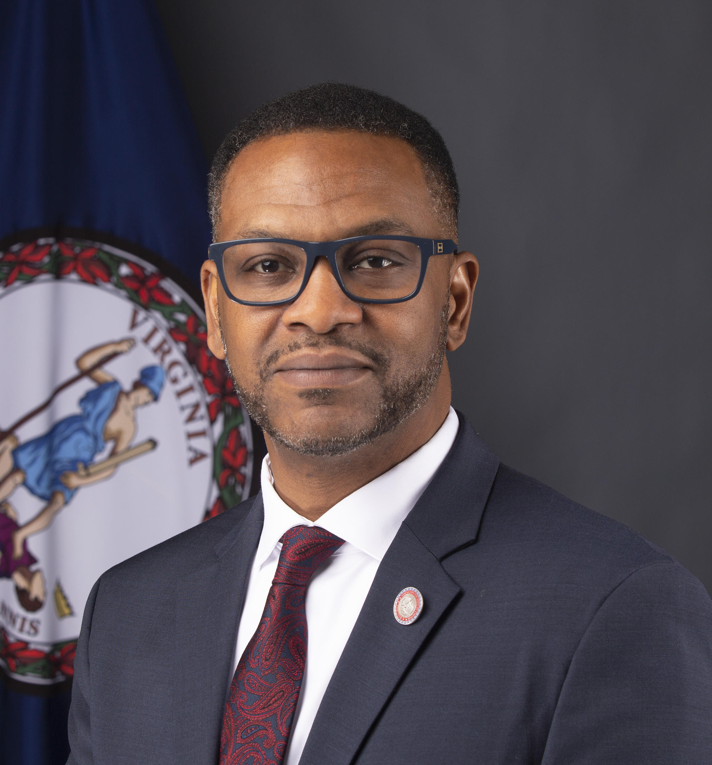 Marcus Thornton, subdirector de datos, viste un traje en su foto y se sienta frente a la bandera de Virginia